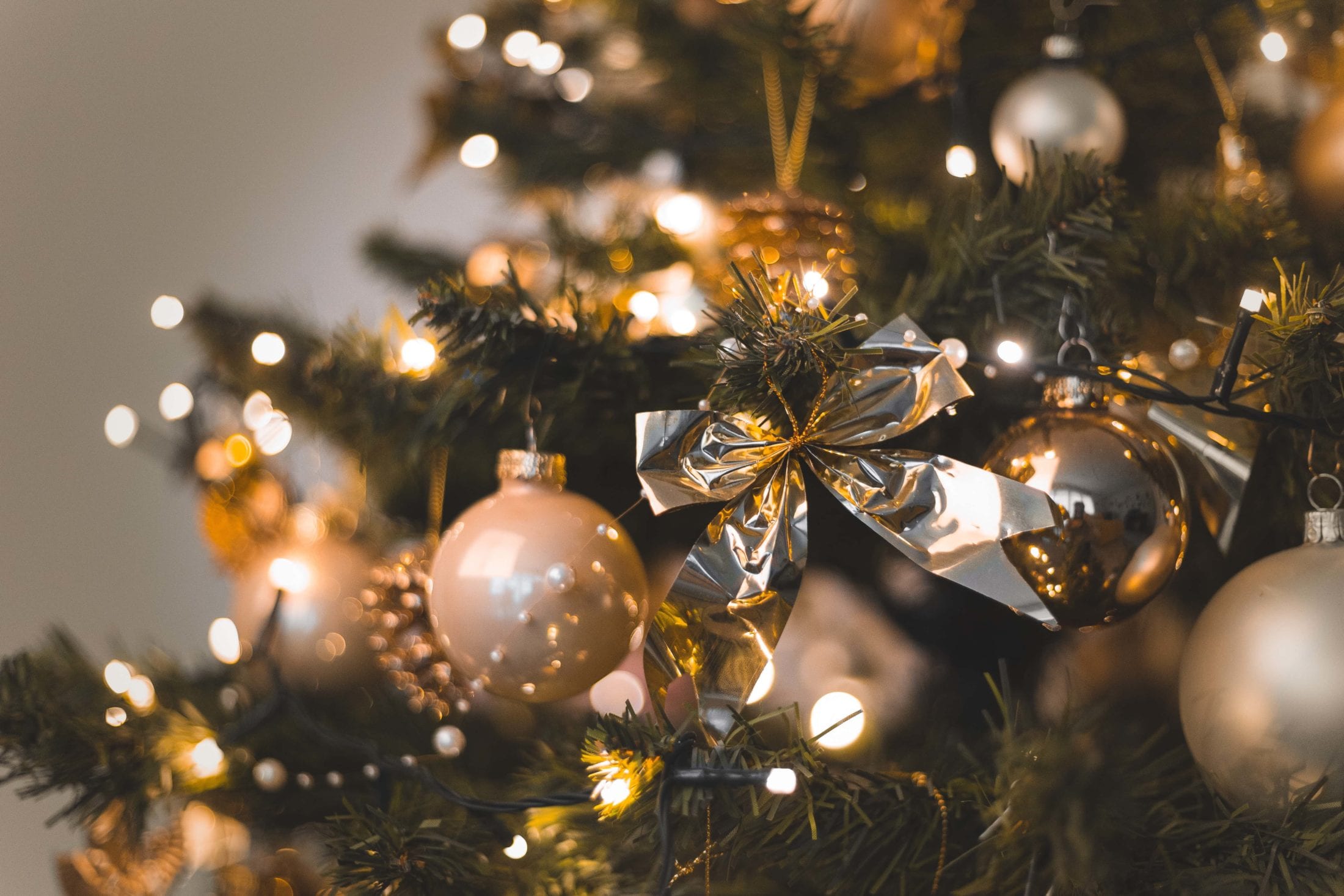 A close-up of a decorated Christmas tree with gold and silver ornaments, a shiny metallic bow, and warm white string lights creating a festive glow—perfect for celebrating the season or highlighting a special Christmas New Year offer.